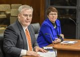 Craig Clark sits at the testifiers' table and looks at someone out of view. Representative Poppe sits beside him and looks in the same direction.